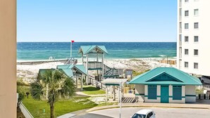 A beachfront hotel with a view of the ocean, a palm tree, and a beach. - Azure #323 (Fort Walton Beach)