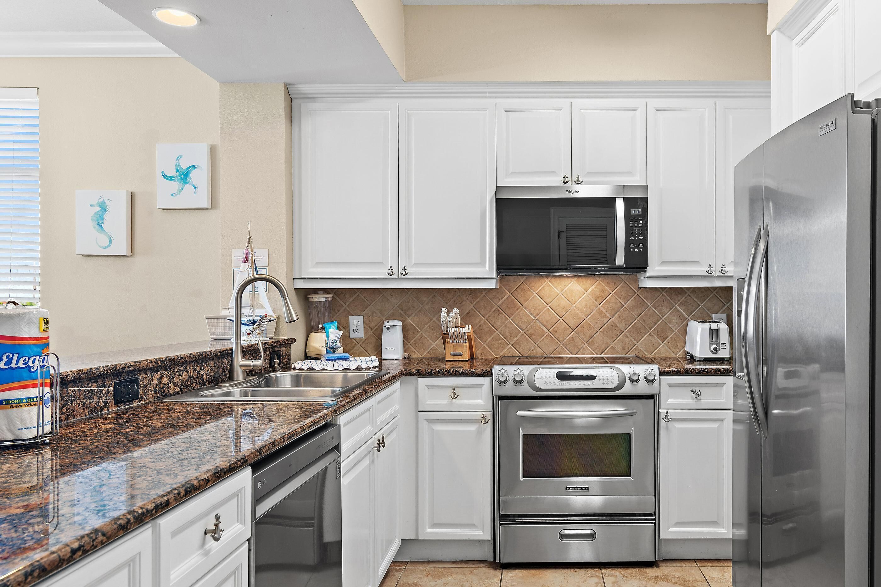 A kitchen with white cabinets, a stainless steel refrigerator, a microwave, an oven, and a granite countertop.