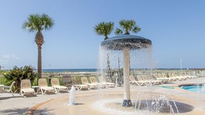 A poolside area with a water fountain, lounge chairs, palm trees, and a clear view of the ocean. - Azure #323 (Fort Walton Beach)