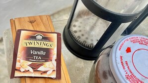 Eine Packung Twinings Vanille Tee, eine French-Press-Kaffeemaschine und ein Kaffeeglas auf einer Holztischplatte.