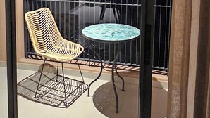 Un balcone con una sedia, un tavolo, una ringhiera e vista sulla città al crepuscolo.