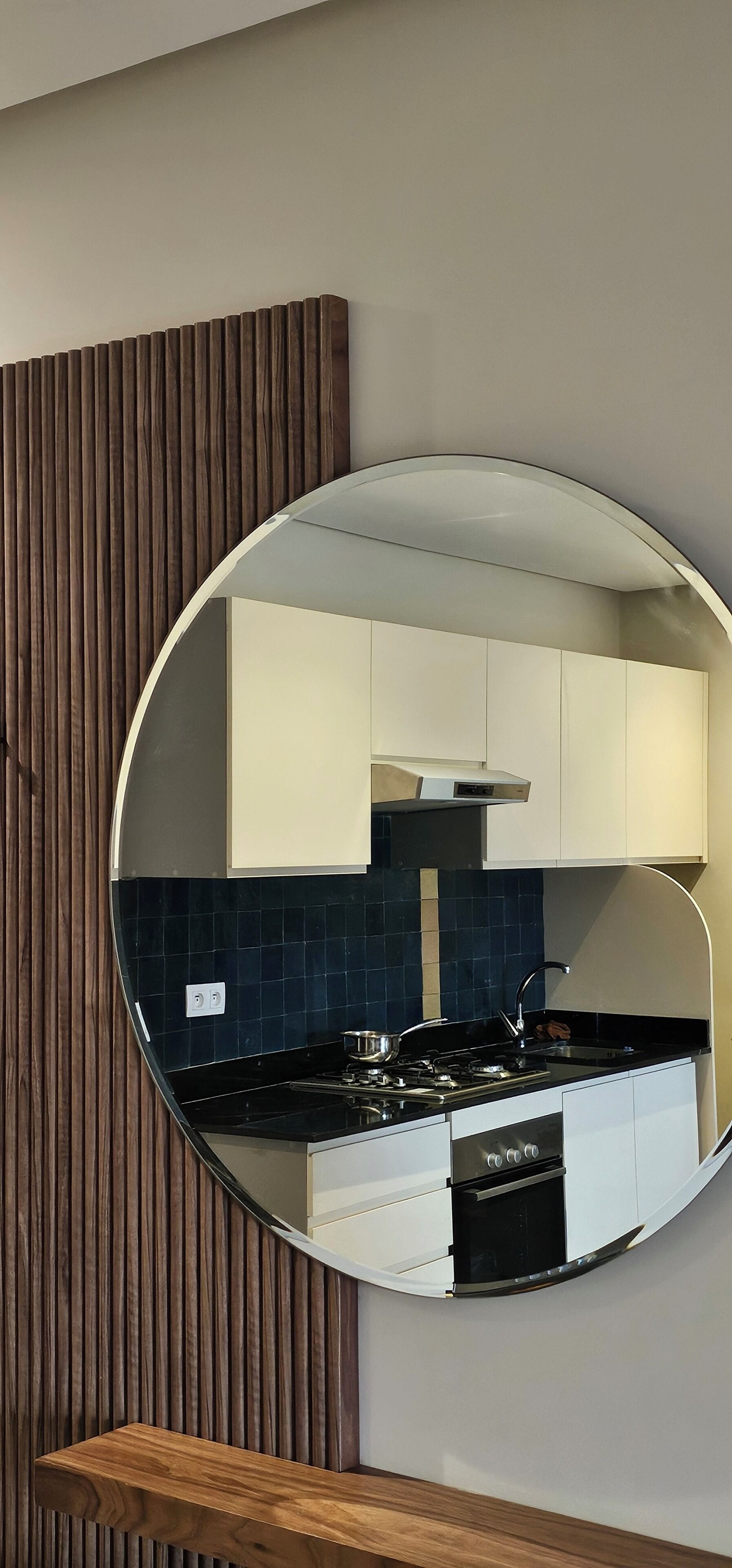 A modern kitchen with white cabinets, a black countertop, and a round mirror on the wall.