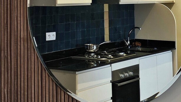 Una cucina moderna con mobili bianchi, un piano di lavoro nero e uno specchio rotondo a parete.