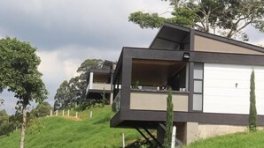 A modern two-story house with a flat roof, large windows, and a grassy hillside setting. - Colina Haus Glampling en Armenia (Armenia)