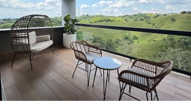 A balcony with wicker furniture, a cushioned chair, and a potted plant. - Colina Haus Glampling en Armenia (Armenia)