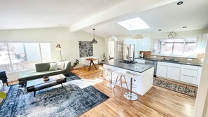 A modern kitchen with white cabinets, a central island, and a dining area with a sofa and chairs. - Bright & Open 2 Bed, Home Walk to Downtown & CU (Boulder)