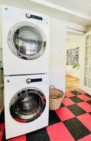 A laundry room with two stacked front-loading washing machines, a wicker basket, and a checkered floor. - Bright & Open 2 Bed, Home Walk to Downtown & CU (Boulder)