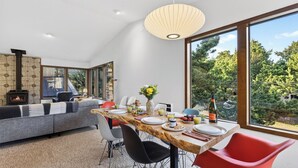A modern dining area with a large window, a fireplace, and a view of the outdoors. - Magic Tree House by Avantstay Fire Pit + Deck + Movie Room Walk to the Beach (Manzanita)