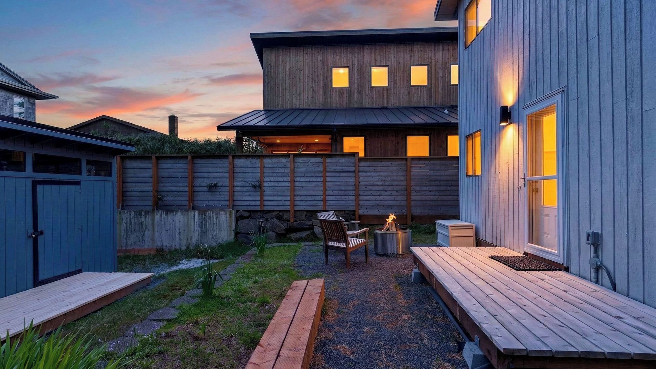 A modern house with a wooden deck, a fire pit, and a patio area.