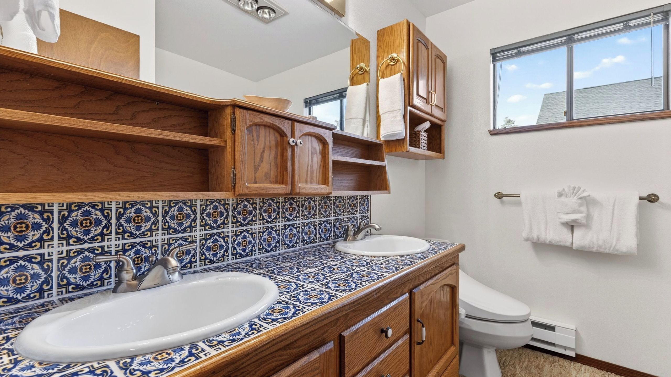 Un baño con dos lavamanos, armarios de madera, un inodoro y una ventana con vistas.