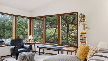 A room with large windows, a black leather chair, a wooden bench, and a bookshelf with books.