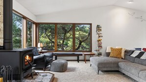 A cozy living room with a fireplace, a sofa, a bench, and a bookshelf. - Magic Tree House by Avantstay Fire Pit + Deck + Movie Room Walk to the Beach (Manzanita)