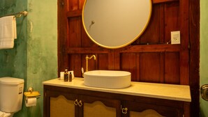 Et badeværelse med et trækommode, et rundt spejl og et toilet.