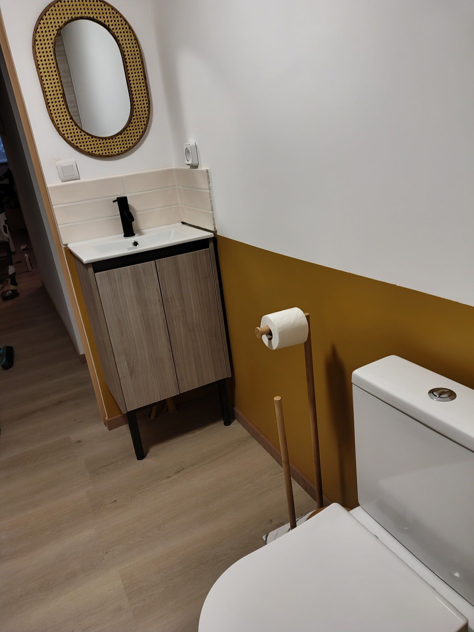 Un baño con inodoro, lavamanos, espejo y soporte para papel higiénico.