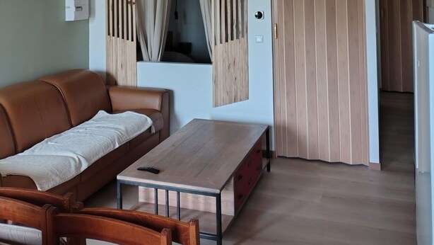 A room with a wooden ceiling, a brown leather sofa, a wooden table, and a door with vertical blinds. - Holiday rental near La Tranche sur mer (La Jonchère)