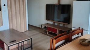 A room with a wooden ceiling, a TV on a wooden stand, a dining table with chairs, and a refrigerator. - Holiday rental near La Tranche sur mer (La Jonchère)