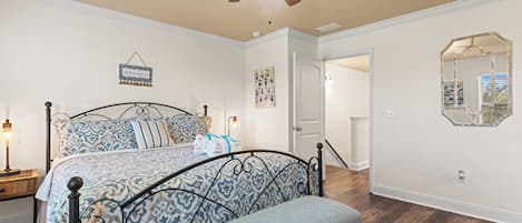 Ein Schlafzimmer mit Bett, einer Bank, einem Deckenventilator, einem Spiegel und einer Tür zu einem anderen Raum.