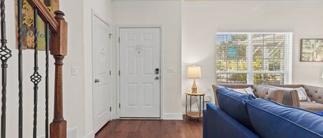 Una habitación con una escalera de madera, una puerta blanca, un sofá azul y una ventana con persianas.