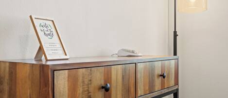 A wooden cabinet with a framed sign, a telephone, and a floor lamp against a plain wall.