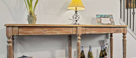 A wooden table with a lamp, a potted plant, a framed picture, and a stack of books.