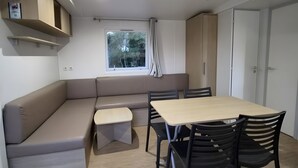 Uma sala de estar moderna com sofá, mesa de jantar e cadeiras. Há uma janela com cortinas, uma luminária no teto e prateleiras embutidas.
