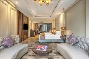 Une chambre d’hôtel comprenant un lit, deux canapés, une table basse, un téléviseur et un lustre.