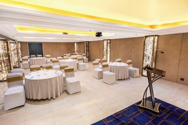 Un salón de conferencias con varias mesas redondas, sillas blancas y un atril.