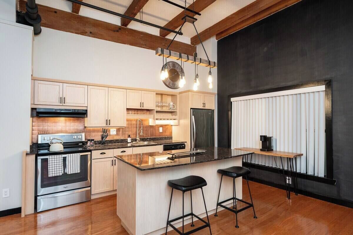 A modern kitchen with a central island, bar stools, and a large window.