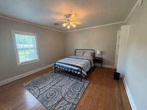 A bedroom with a bed, a nightstand, a ceiling fan, a window, and a patterned rug.
