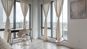 Habitació moderna amb grans finestres, una taula, una cadira i vista a la ciutat.
