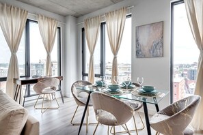 A modern dining area with a glass table, matching chairs, and a city view. - Skyline Penthouse | 360° Views (Montreal)