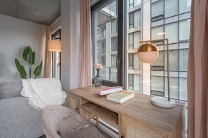Un salon moderne avec un bureau en bois, un canapé confortable, une lampe sur pied et une grande fenêtre donnant sur la ville.