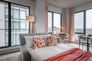 A modern hotel room with a large bed, a desk, and a view of the city. - Skyline Penthouse | 360° Views (Montreal)