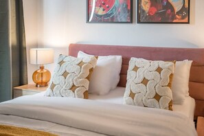 Une chambre d’hôtel avec un lit, deux oreillers, une table de chevet avec une lampe et deux tableaux abstraits accrochés au mur.