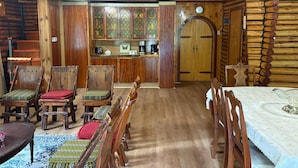 A rustic log cabin interior with a dining area, wooden chairs, a table, a bar area with a coffee machine, and a clock on the wall. - Chalet Lumière Chalet Lumière (Rawdon)
