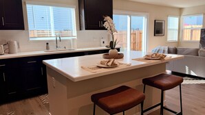 A modern kitchen with dark cabinets, a white countertop, and a central island with stools. - Spacious 3-bedroom New house , Feel at home (Turlock)