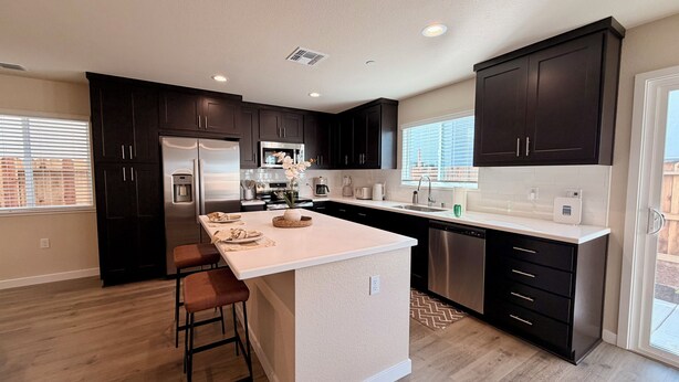 A modern kitchen with dark cabinets, stainless steel appliances, a large island with stools, and a dishwasher. - Spacious 3-bedroom New house , Feel at home (Turlock)