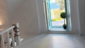 A room with a sloped ceiling, a window with an open shutter, and a potted plant on the windowsill.