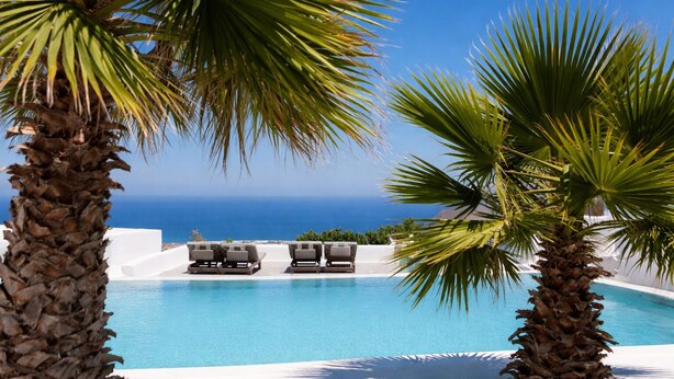 A pool with lounge chairs, palm trees, and a view of the ocean.