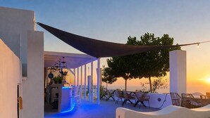 A modern outdoor patio area with a seating arrangement, a pathway leading to a covered area, and a view of the sunset.