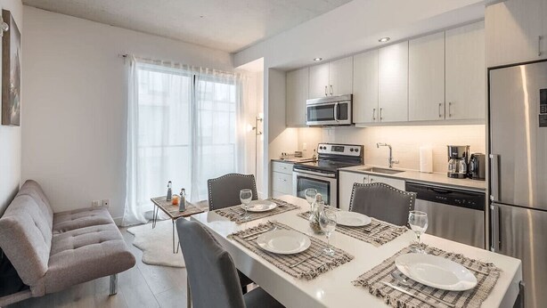 Une cuisine moderne avec des meubles blancs, un réfrigérateur en acier inoxydable et un coin repas avec une table dressée pour quatre personnes.