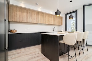A modern kitchen with dark cabinetry, a central island, and bar stools. - 'The Caletas Village Luxury' with Sea Views and Baviera Golf Course Scenery (Vélez-Málaga)