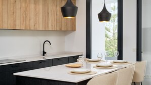 Ett modernt kök med en stor köksö, svarta hänglampor och utsikt genom ett stort fönster.