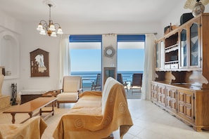 Un salon avec un canapé, des fauteuils, un meuble en bois et une vue sur la mer.