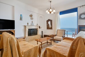 Una camera d'albergo con TV, camino, divano, poltrona e un balcone con vista.
