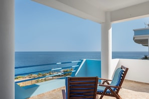 Un balcon avec vue sur la mer, une chaise en bois et une rambarde bleue.