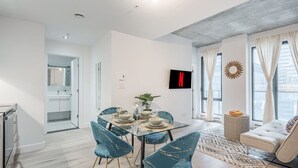 Ein modernes Wohnzimmer mit Essbereich, einem an der Wand montierten Fernseher und einem großen Fenster mit Vorhängen.