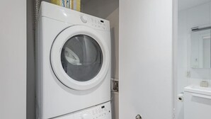 Eine Waschmaschine und ein Trockner, beide mit Frontöffnung, stehen in einem Hauswirtschaftsraum mit einem weißen Waschbecken und Spiegel.