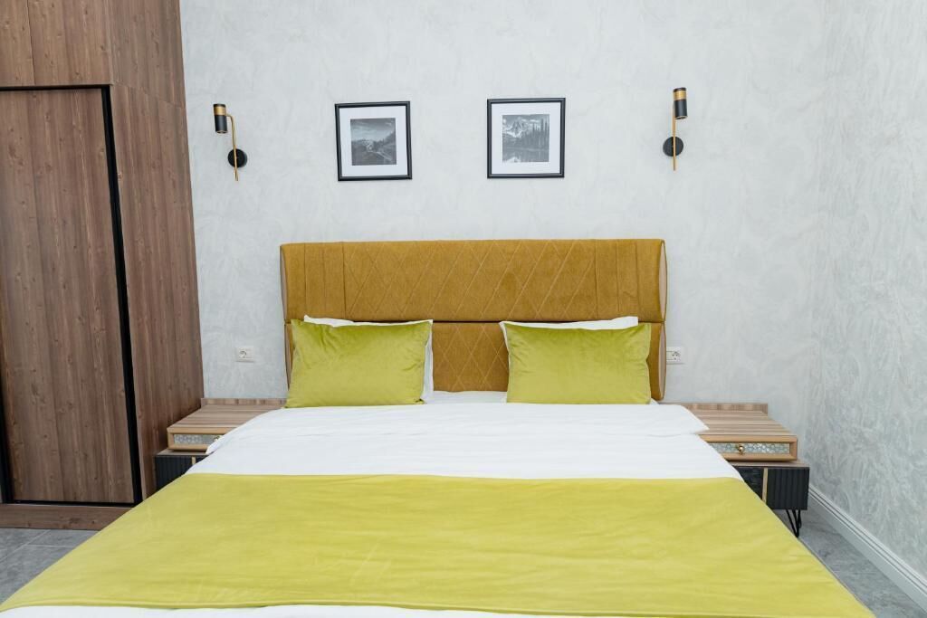 Habitación de hotel con una cama, dos mesitas de noche, un armario de madera y dos cuadros en la pared.