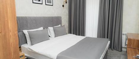 Una habitación de hotel moderna con una cama grande, ropa de cama gris, una mesita de noche de madera y una lámpara de pared.